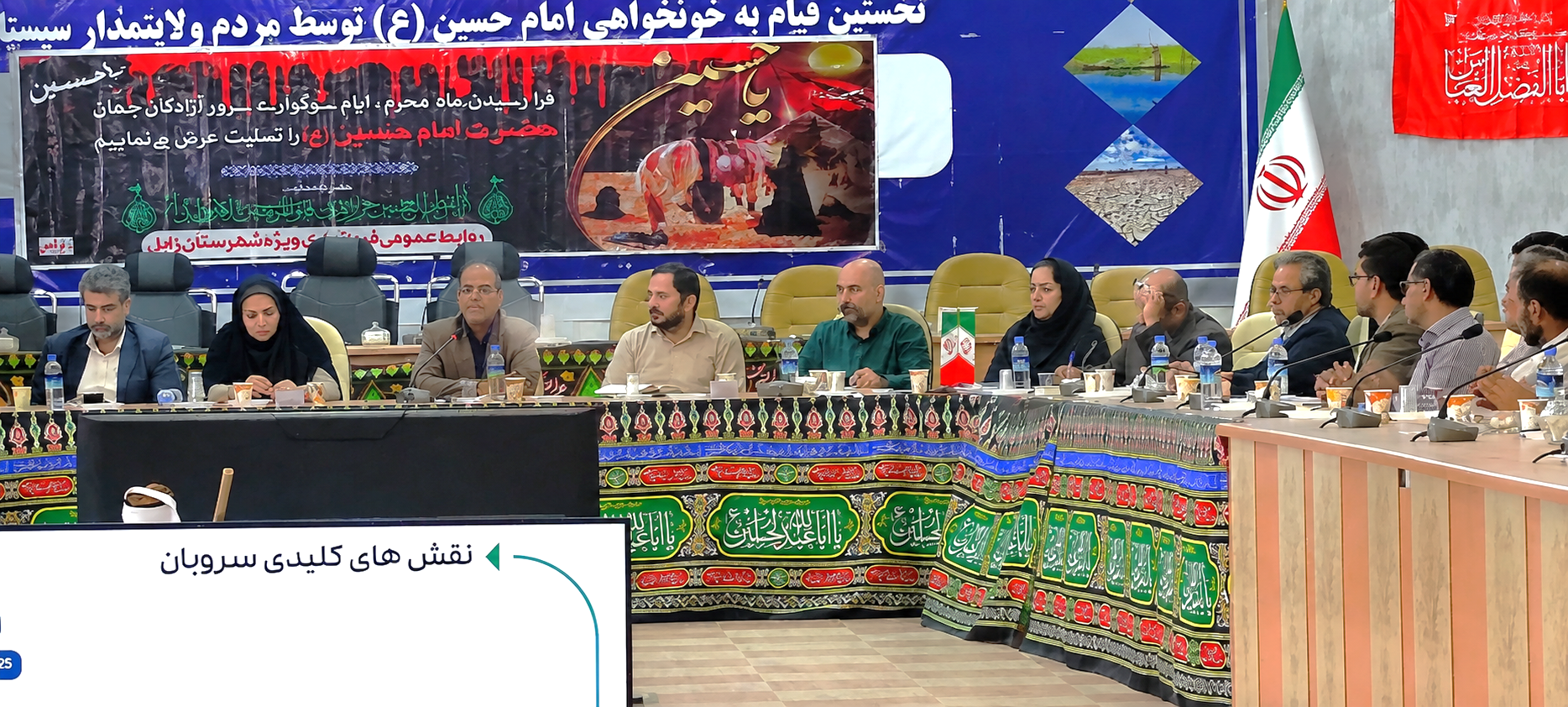 جلسه رسمی و جمعی از مسئولان و شرکت‌کنندگان در سالن کنفرانس با بنر مذهبی، پرچم ایران و اسلاید «نقش‌های کلیدی سروبان» در پیش‌زمینه